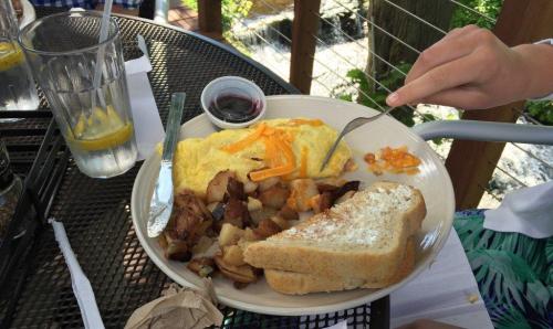 A plate of breakfast featuring an omelet with cheese, seasoned potatoes, toast, and a small cup of jelly.
