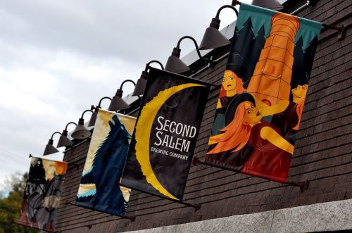 Banners for Second Salem Brewing Company featuring colorful, artistic designs hanging from a building.