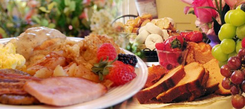 A delicious spread featuring breakfast items, fruits, and baked goods, surrounded by colorful flowers.