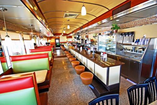 A retro diner interior featuring colorful booths, a long counter, and a display case, with a bright and inviting atmosphere.
