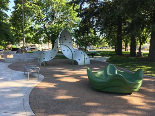 A playground featuring a unique climbing structure and a green seating area, surrounded by trees and open space.