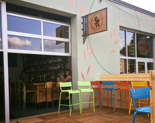 A colorful outdoor seating area in front of a bar with large windows and a wooden counter inside.