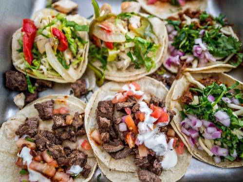 A variety of tacos filled with beef, vegetables, and toppings, arranged on a metal tray.