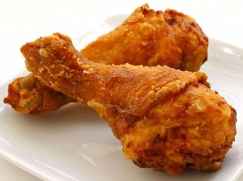 Two crispy, golden-brown fried chicken drumsticks on a white plate.