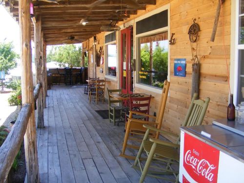 A rustic wooden porch with rocking chairs and a Coca-Cola cooler, surrounded by greenery.