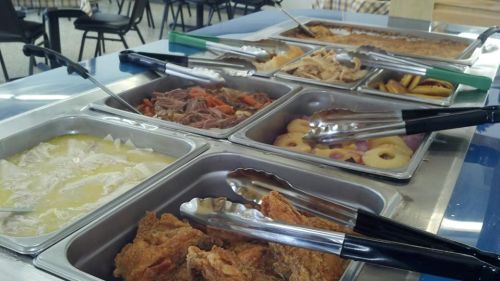 A buffet spread featuring various dishes, including fried chicken, meats, vegetables, and desserts, with serving tongs.
