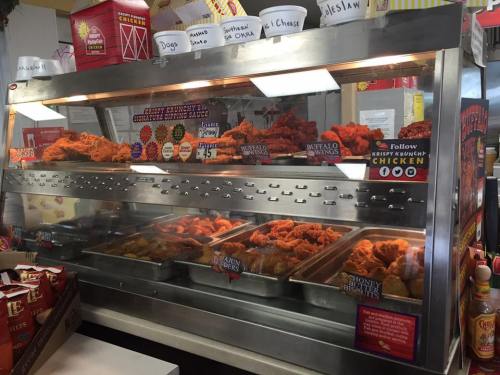 A display case filled with various types of fried chicken, including buffalo and honey butter, in a fast-food setting.