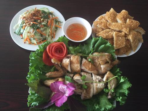A vibrant meal featuring roasted chicken, crispy dumplings, fresh salad, and dipping sauce, garnished with herbs and flowers.