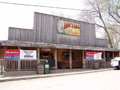 A rustic wooden bar with a sign reading "Don's Bar," featuring banners for Budweiser and Bud Light outside.