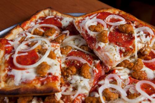 A close-up of a pizza topped with pepperoni, sausage, onions, and melted cheese on a wooden table.