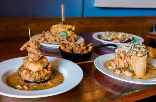 A variety of dishes including fried shrimp, gumbo, and a casserole, served on white plates and a cast iron skillet.