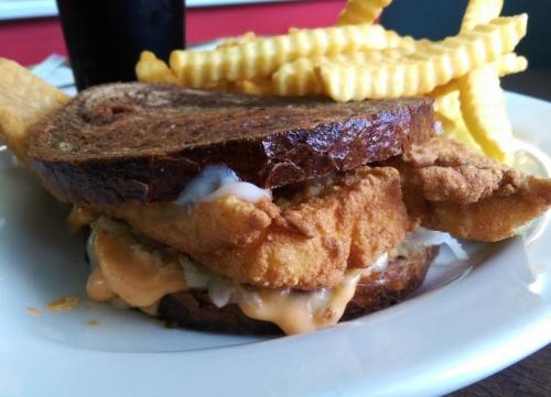 A crispy fried chicken sandwich on toasted bread, served with crinkle-cut fries on the side.