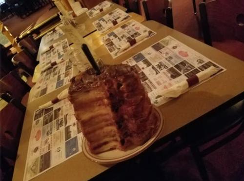 A large, multi-layered cake with frosting sits on a table set with menus and utensils in a restaurant.