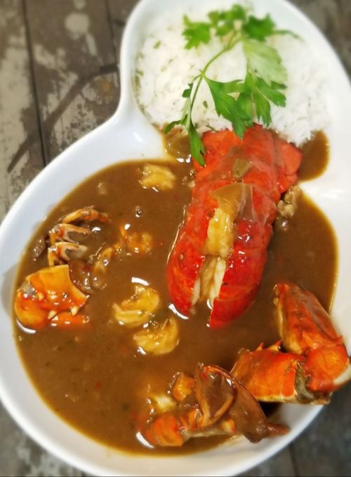 A plate of lobster in a rich sauce, served with rice and garnished with a sprig of parsley.