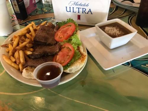 A plate with sliced beef, lettuce, tomatoes, fries, and a small bowl of rice with gravy on a colorful table.
