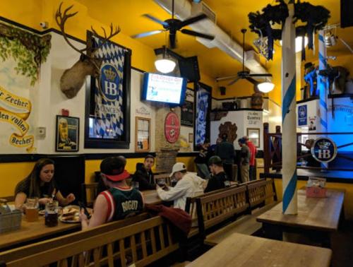 A lively restaurant interior with wooden benches, Bavarian decor, and patrons enjoying food and drinks.
