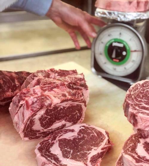 A hand reaches for a scale next to several cuts of marbled beef on a countertop.