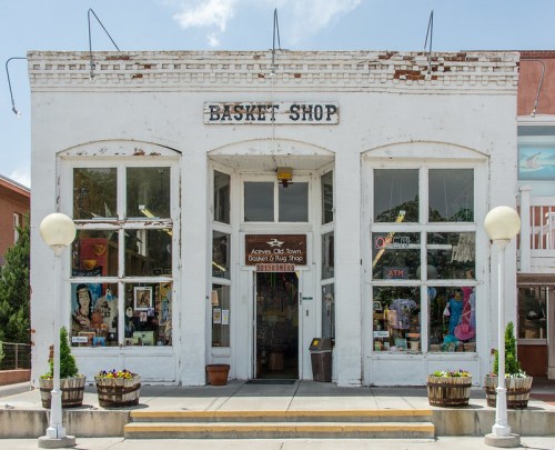 A charming white building with "Basket Shop" sign, featuring large windows and potted plants at the entrance.