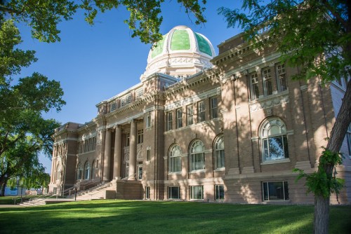 Historic building with a green dome, large windows, and surrounding trees on a sunny day.