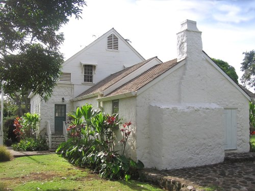 A charming white cottage surrounded by lush greenery and colorful flowers under a clear blue sky.