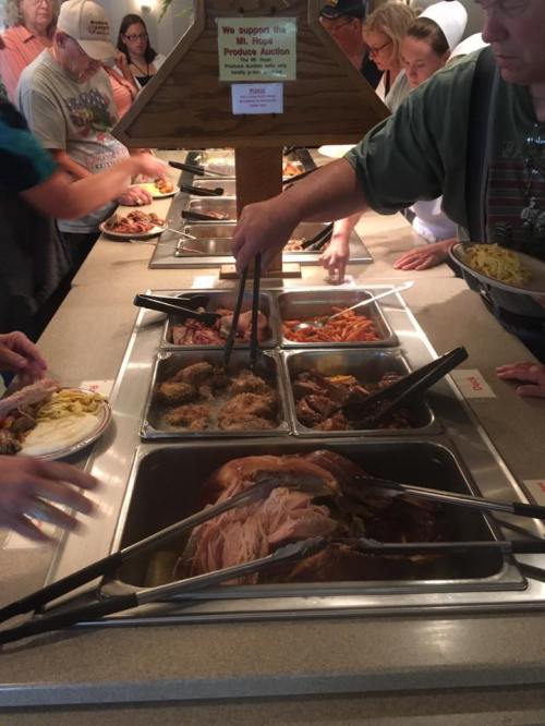 A buffet line with people serving themselves various dishes, including meats and sides, in a casual dining setting.