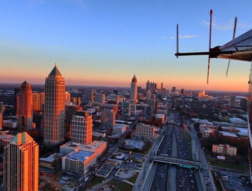 Aerial view of a city skyline at sunset, featuring tall buildings and a busy highway below.