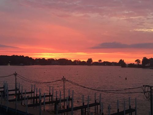 A vibrant sunset over a calm lake, with silhouettes of docks and trees against a colorful sky.