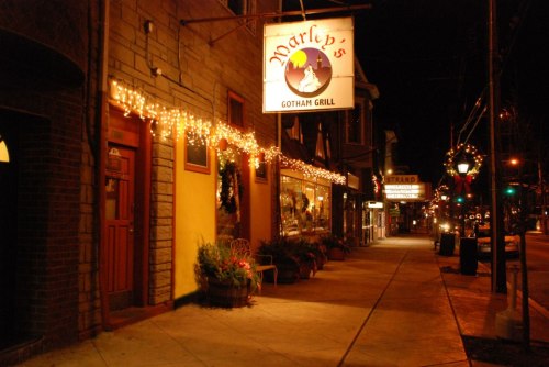 A cozy restaurant exterior at night, adorned with string lights and festive decorations, along a charming street.