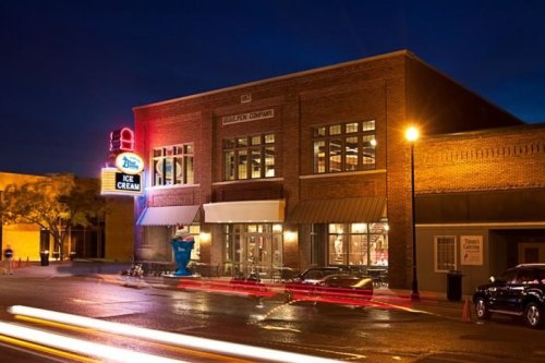 A brightly lit ice cream shop at night, featuring a neon sign and a brick facade, with light trails from passing cars.