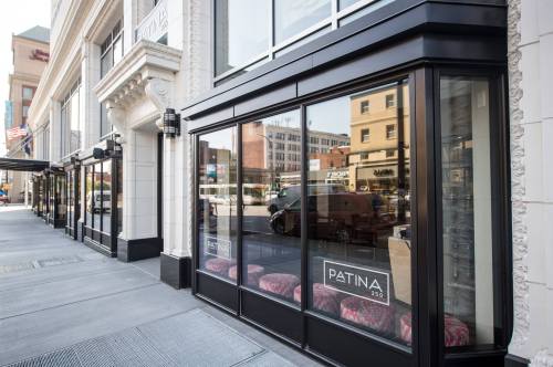 Exterior view of Patina 452 restaurant, featuring large glass windows and colorful seating outside.