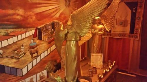 Golden angel statues with wings, set against a colorful backdrop featuring a historical scene and decorative elements.