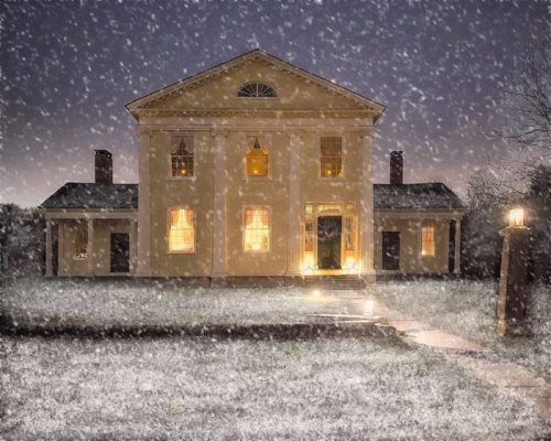 A snow-covered house at night, warmly lit from within, with snowflakes falling gently around it.