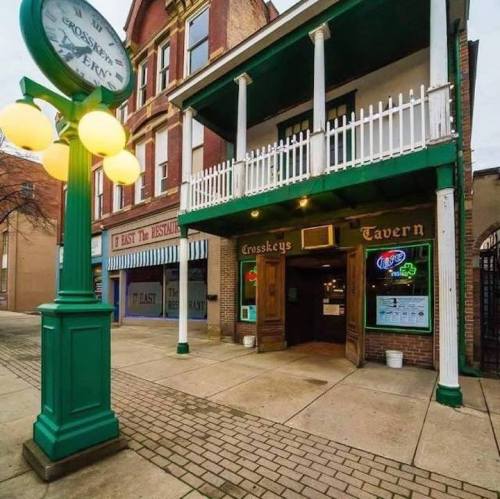 Exterior of Crosskeys Tavern with green accents, a clock nearby, and a brick walkway in a quaint urban setting.