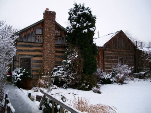 A snowy scene featuring a cozy wooden house surrounded by snow-covered trees and a winter landscape.