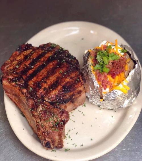 A grilled steak with char marks served alongside a loaded baked potato topped with cheese and green onions.