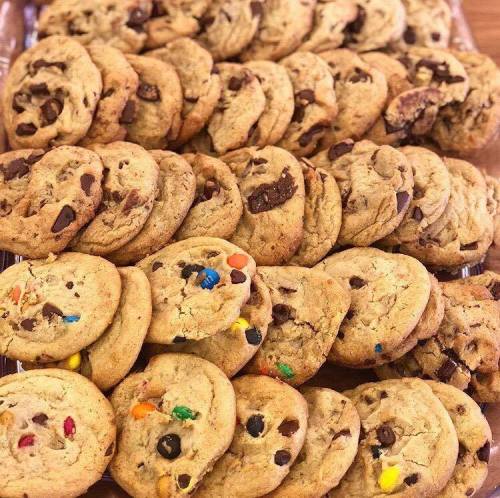 A tray of freshly baked cookies, featuring chocolate chip, M&M, and assorted varieties, arranged neatly.