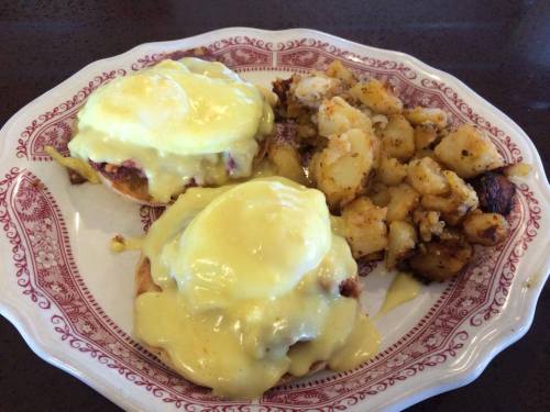 A plate of eggs Benedict topped with hollandaise sauce, served with a side of seasoned, diced potatoes.
