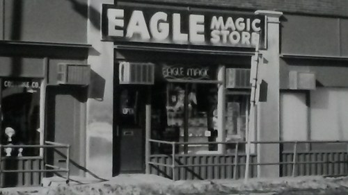 Black and white image of the "Eagle Magic Store" storefront with signage and a railing in front.