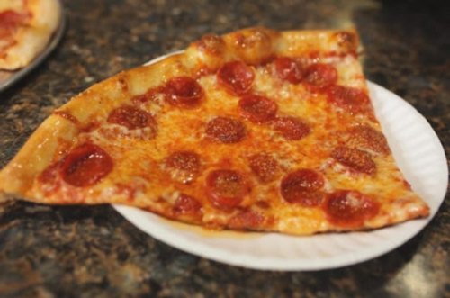 A slice of pepperoni pizza on a white plate, featuring melted cheese and a crispy crust.