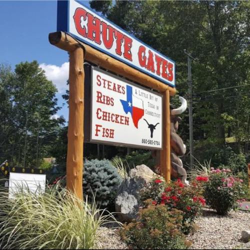 Sign for "Chute Gates" featuring steaks, ribs, chicken, and fish, surrounded by greenery and flowers.