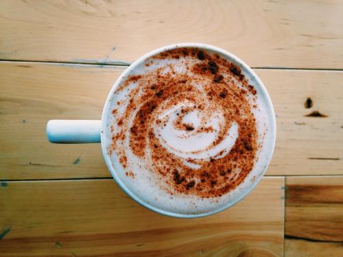 A white mug filled with frothy coffee topped with a swirl of cinnamon on a wooden table.