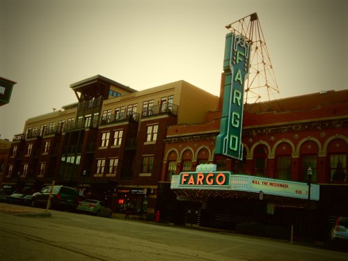 Historic Fargo theater sign with a modern building in the background, bathed in warm evening light.