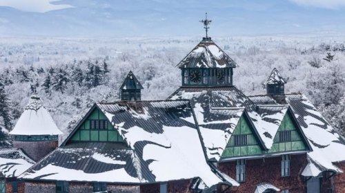 Snow-covered rooftops of a historic building surrounded by a winter landscape of trees and mountains.