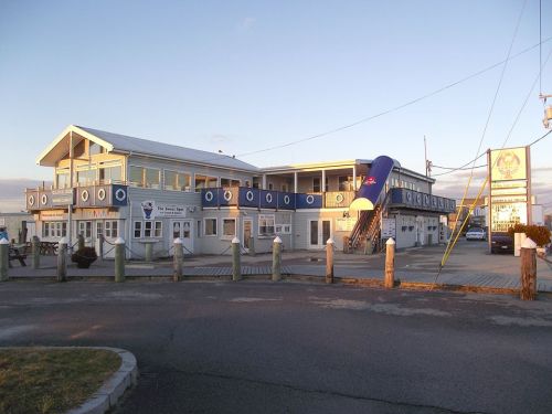 A waterfront building with a blue awning, featuring multiple windows and a staircase, set against a sunset sky.
