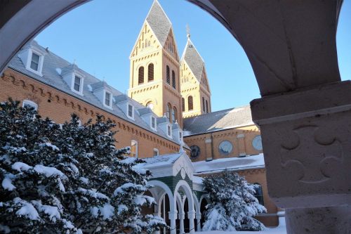 Snow-covered building with twin towers, framed by an arch, under a clear blue sky.