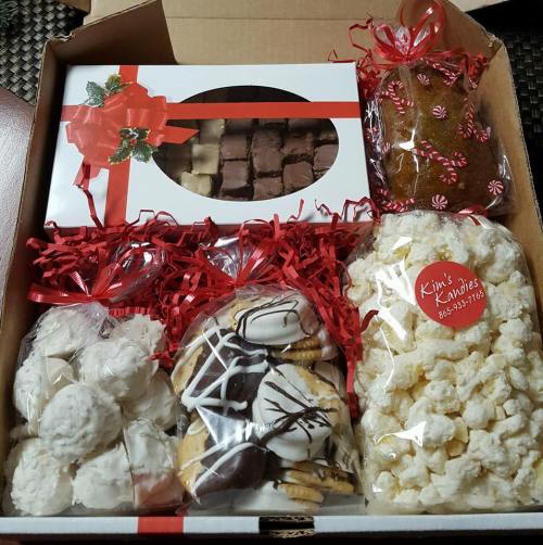 A festive gift box filled with assorted treats: cookies, popcorn, fudge, and a gingerbread loaf, all decorated with ribbons.