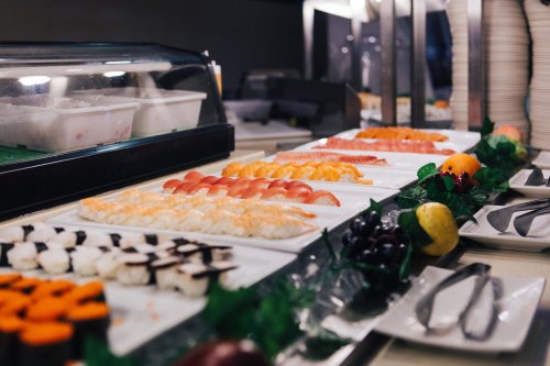 A variety of sushi and sashimi displayed on white plates, with garnishes and utensils in a buffet setting.