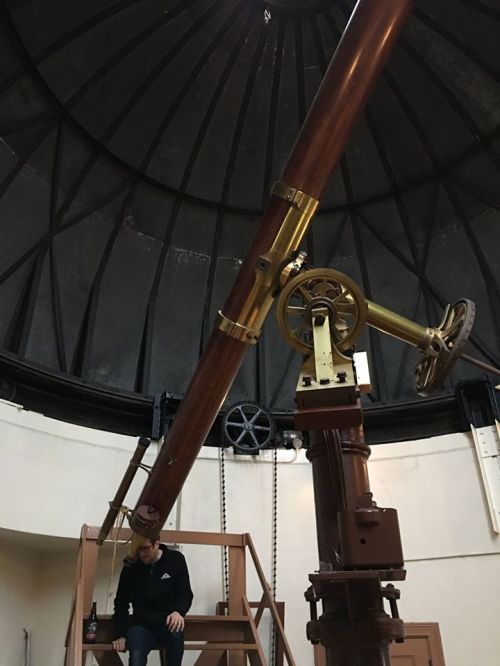 A person sits near a large, vintage telescope inside a domed observatory.