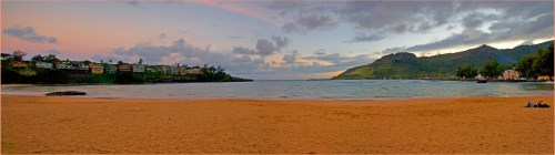A serene beach at sunset, with gentle waves, lush hills in the background, and a few clouds in the sky.