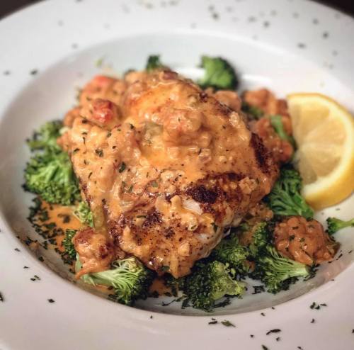 A plate of grilled fish topped with a creamy sauce, served on a bed of broccoli and garnished with a lemon wedge.